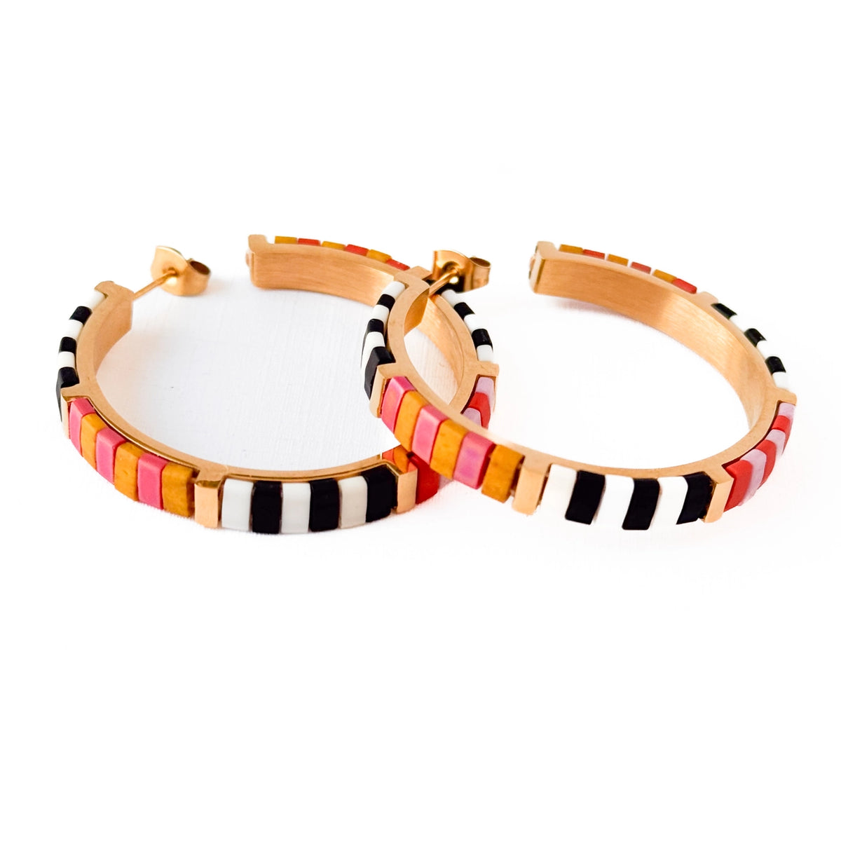 A pair of gold hoop earrings decorated with alternating rows of colorful rectangular beads in black, white, pink, orange, and yellow, set against a plain white background.